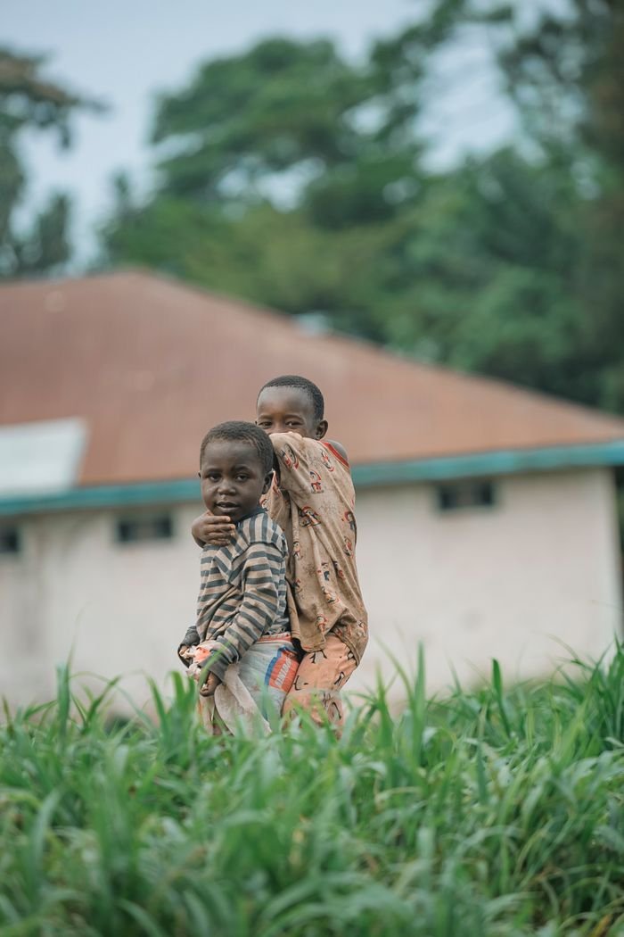 Two children playing outdoors in a village setting, surrounded by lush greenery.