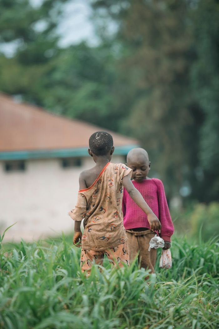 Two children play in a lush green field, showing innocence and joy in a rural setting.