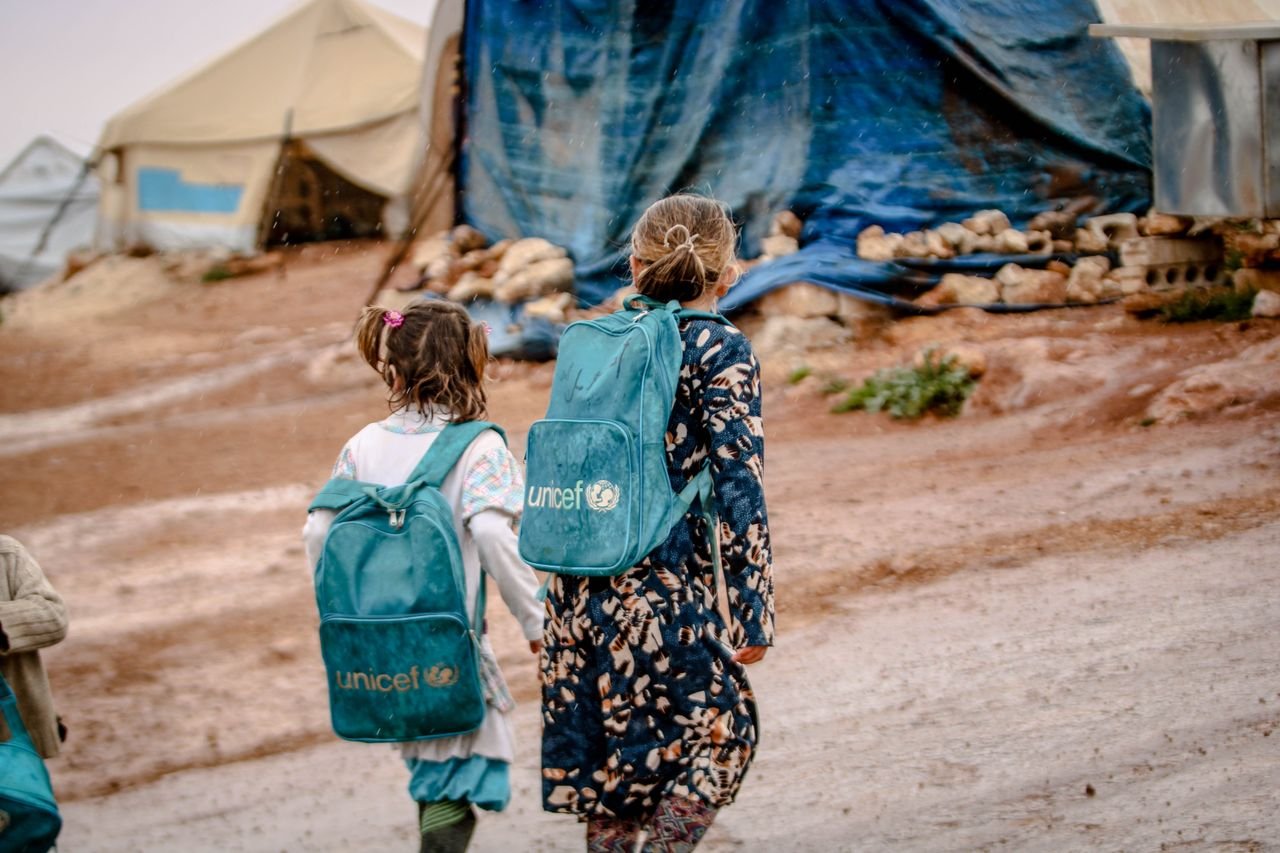 Children at a refugee camp in Syria carrying blue UNICEF backpacks.