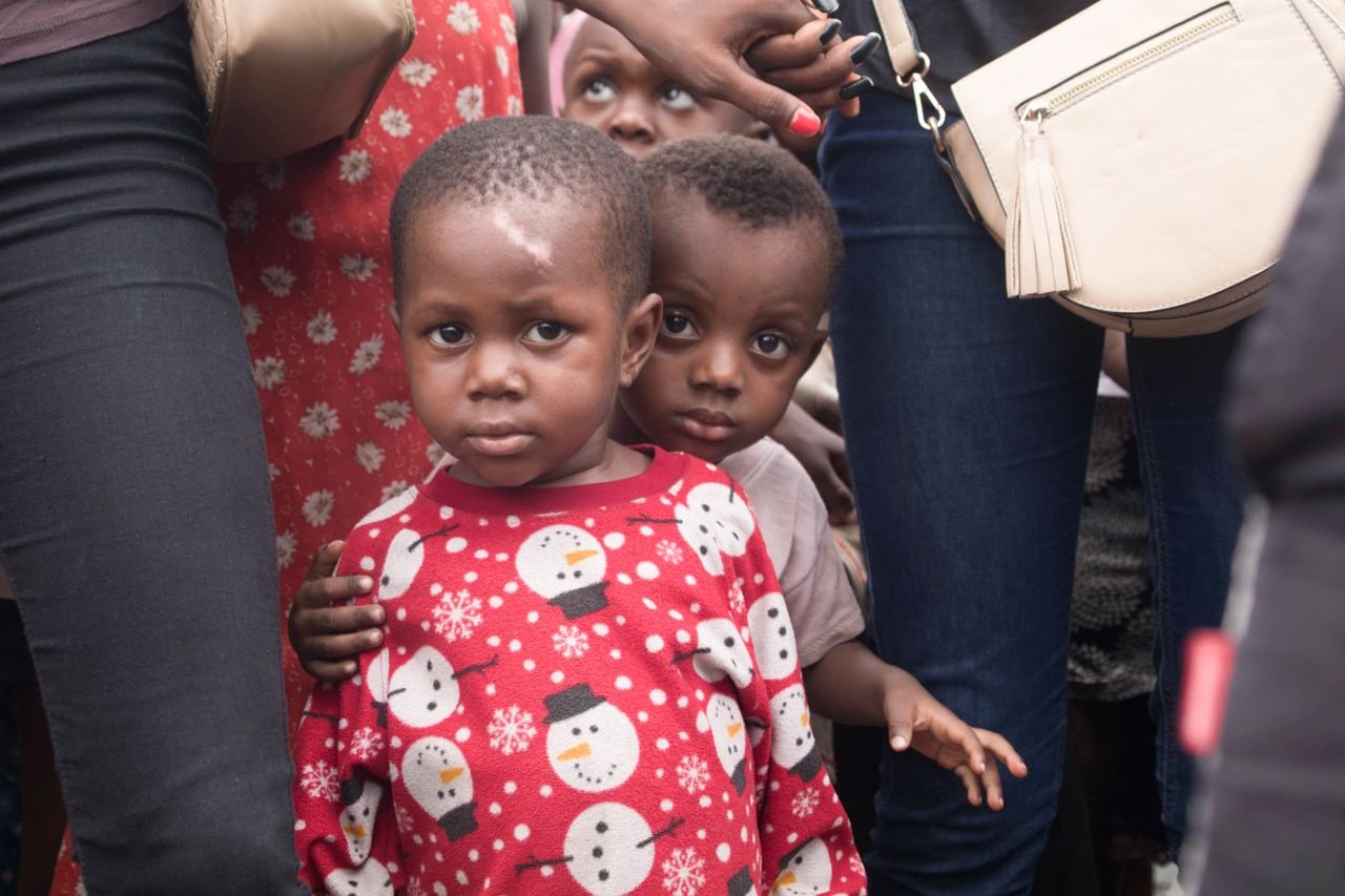 About Two young children in a crowd, wearing a festive red sweater with snowman patterns.